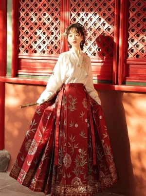 Three-quarter front view of a woman wearing a wine-red Ming Dynasty inspired brocade mamianqun horse face skirt with bamboo floral motifs and a white cross-collar Hanfu blouse