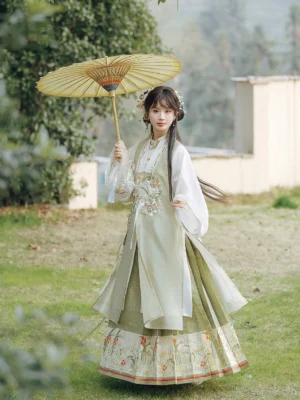 Ming Dynasty spring Hanfu outfit with sage green embroidered vest and mamian skirt photographed outdoors with a yellow oil paper umbrella