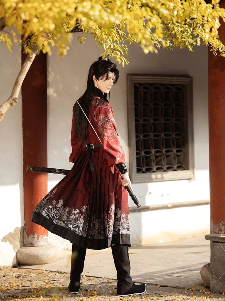Rear view of a male model wearing a crimson Ming Dynasty Hanfu robe with pleated landscape-patterned skirt, black hem border, and sword under autumn foliage