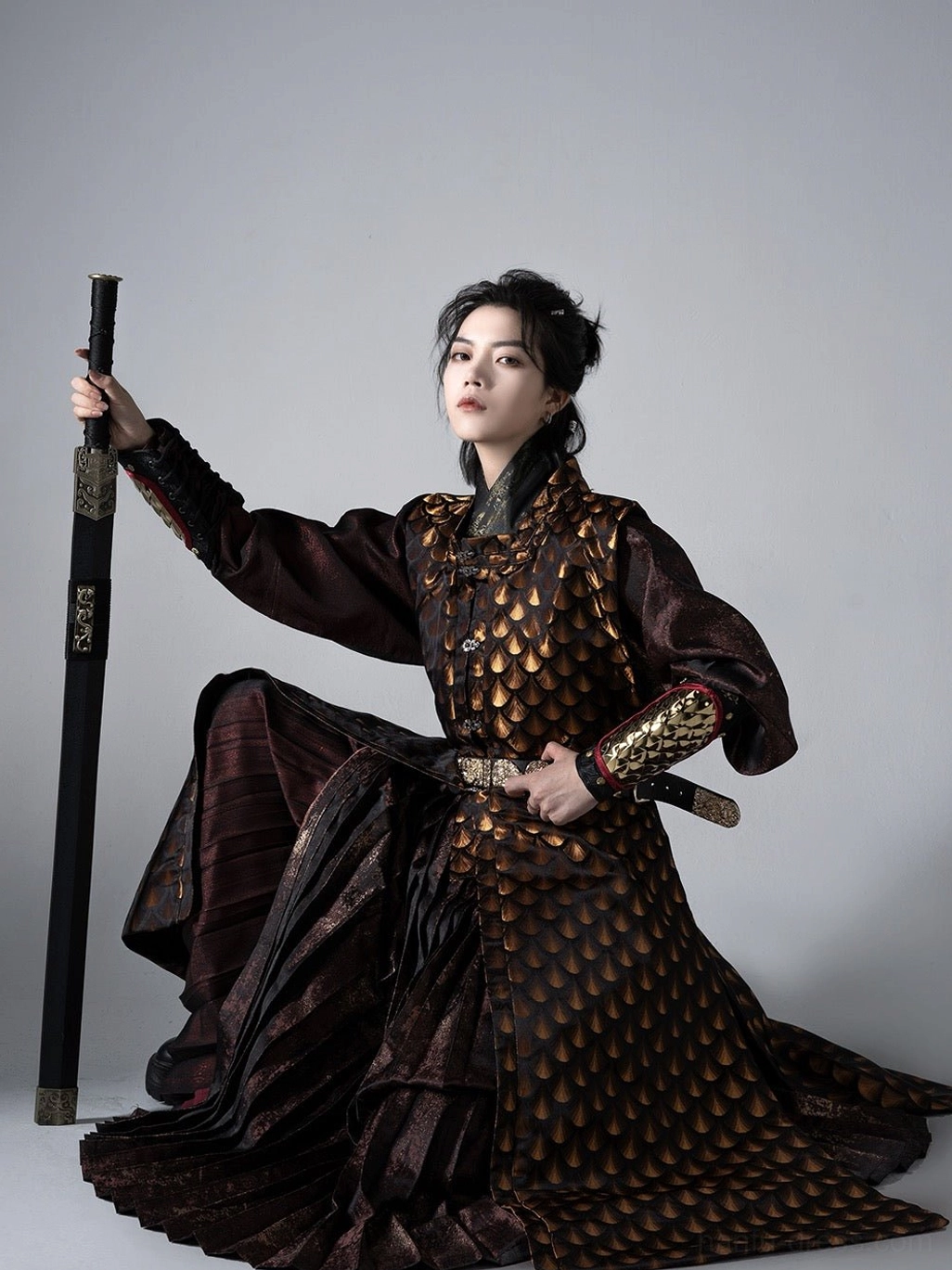 Low angle seated view of a Ming Dynasty Tieli Hanfu warrior wearing a full coverage golden scale patterned robe with traditional Chinese sword