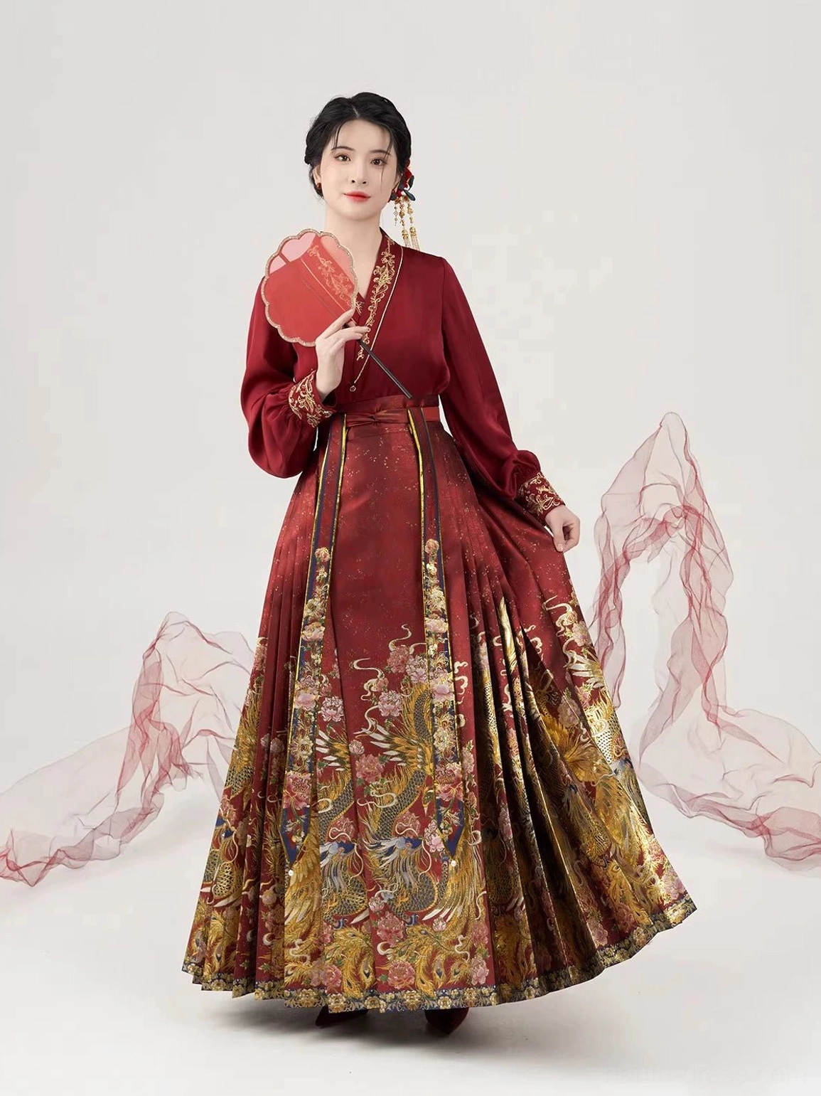 Ming Dynasty wedding Hanfu outfit in a front three-quarter view with a red folding fan and golden phoenix dragon Mamian skirt patterns