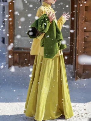 Back side view of green fuzzy Chinese round collar jacket and pale yellow long skirt Ming-inspired Hanfu outfit in falling snow