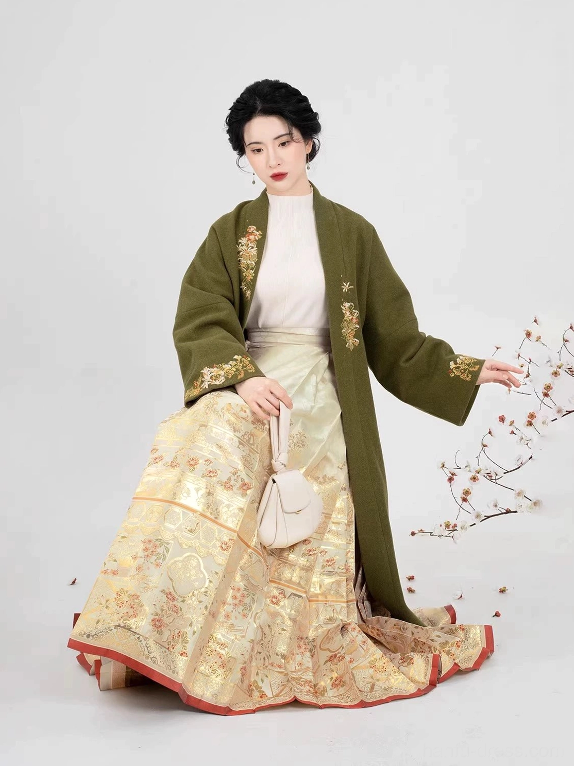 Seated model wearing a complete Ming-inspired hanfu set with an olive-green embroidered coat and gold brocade skirt