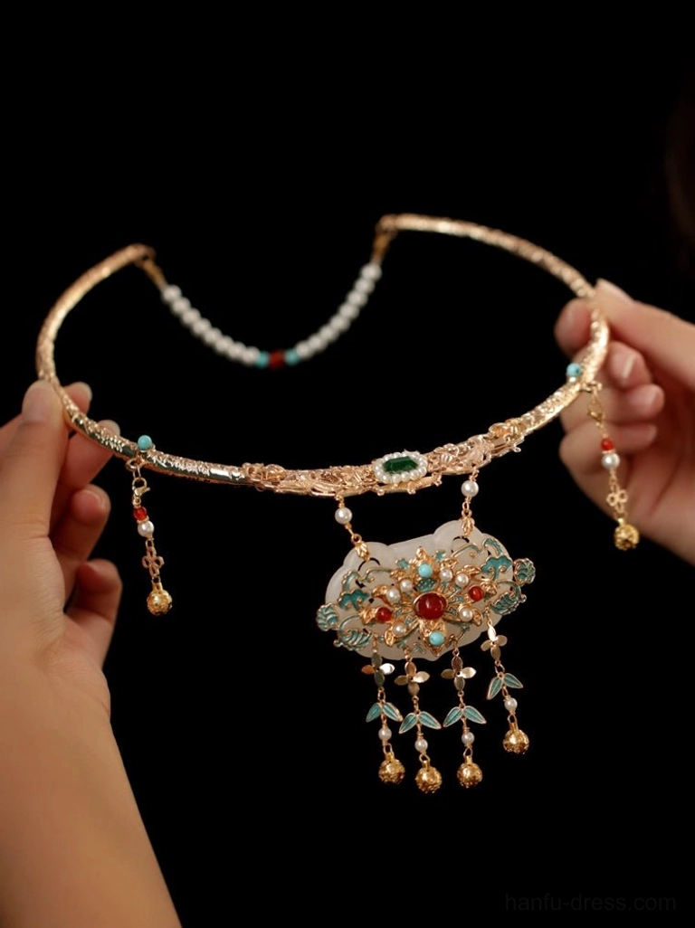 Side-front view of Ming-style wedding necklace with gold-tone metal, pearl forehead-chain detail, white jade-style pendant, enamel gemstone accents, and dangling bell tassels