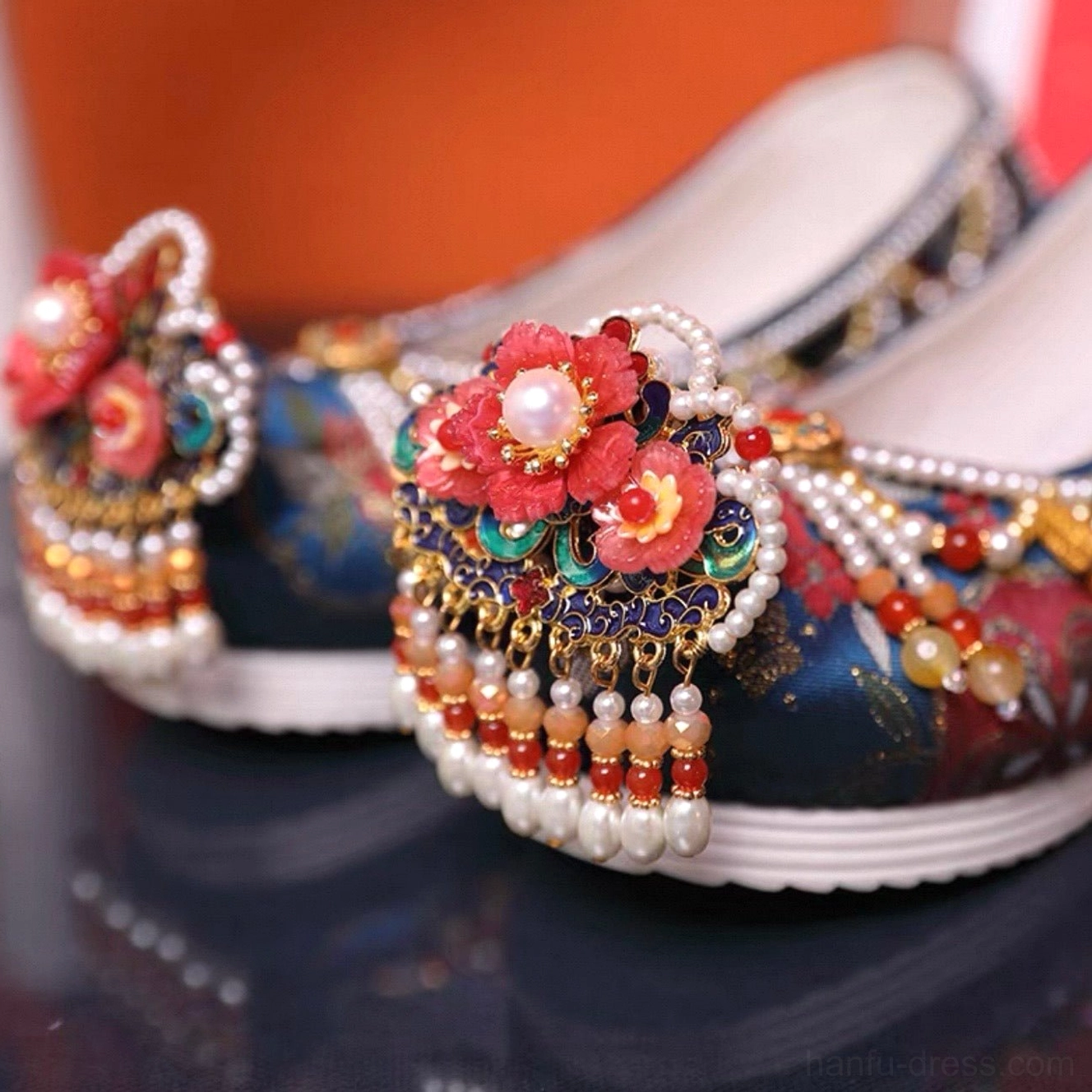 Pair of blue embroidered Chinese Hanfu shoes showing red flower toe ornaments pearl bead tassels metallic floral accents and white platform soles