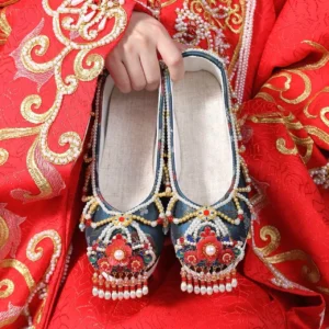 Blue embroidered Hanfu wedding shoes with red floral ornaments pearl tassels and white platform rubber soles displayed with red Xiuhe wedding attire