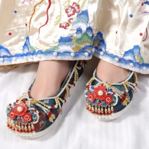 Woman wearing blue Chinese Hanfu shoes with red flower decorations pearl tassels and thick white soles beneath an embroidered traditional skirt