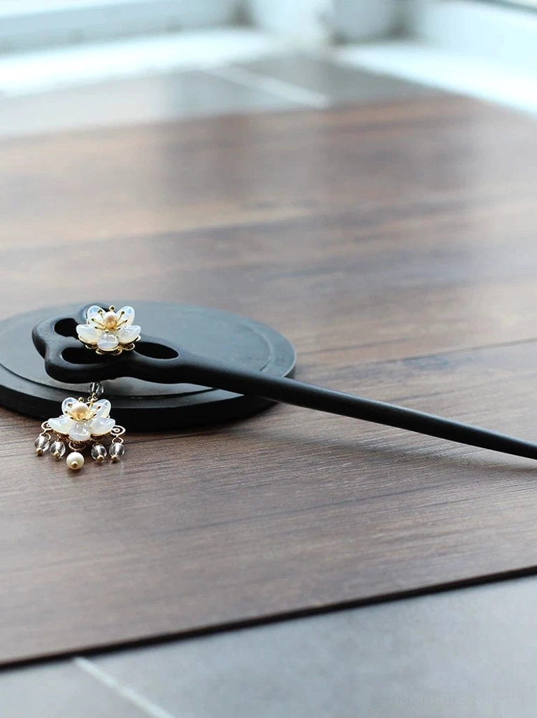 Side view of a minimalist ebony Chinese hairpin with a black wooden handle, small floral ornament, and matching decorative tassel beside a black round tray