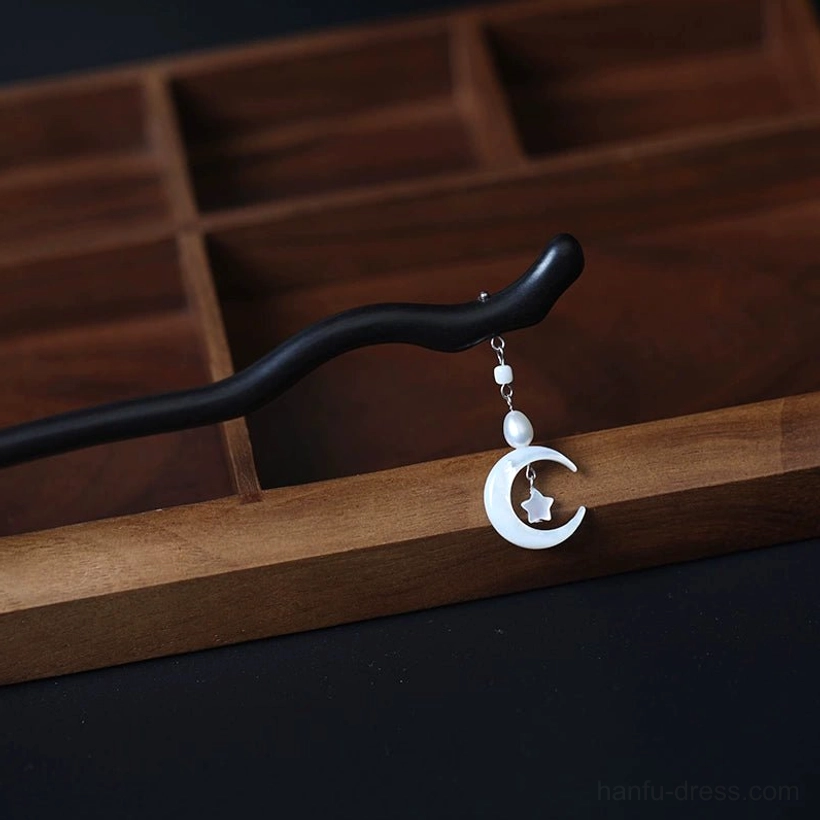 Minimalist dark wavy Chinese hair stick with shell-like crescent moon, star detail, and pearl pendant displayed on a wooden compartment tray