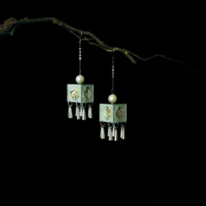 Pair of mint green carved square Hanfu earrings with faux pearl tops silver chains and metal tassels on black background