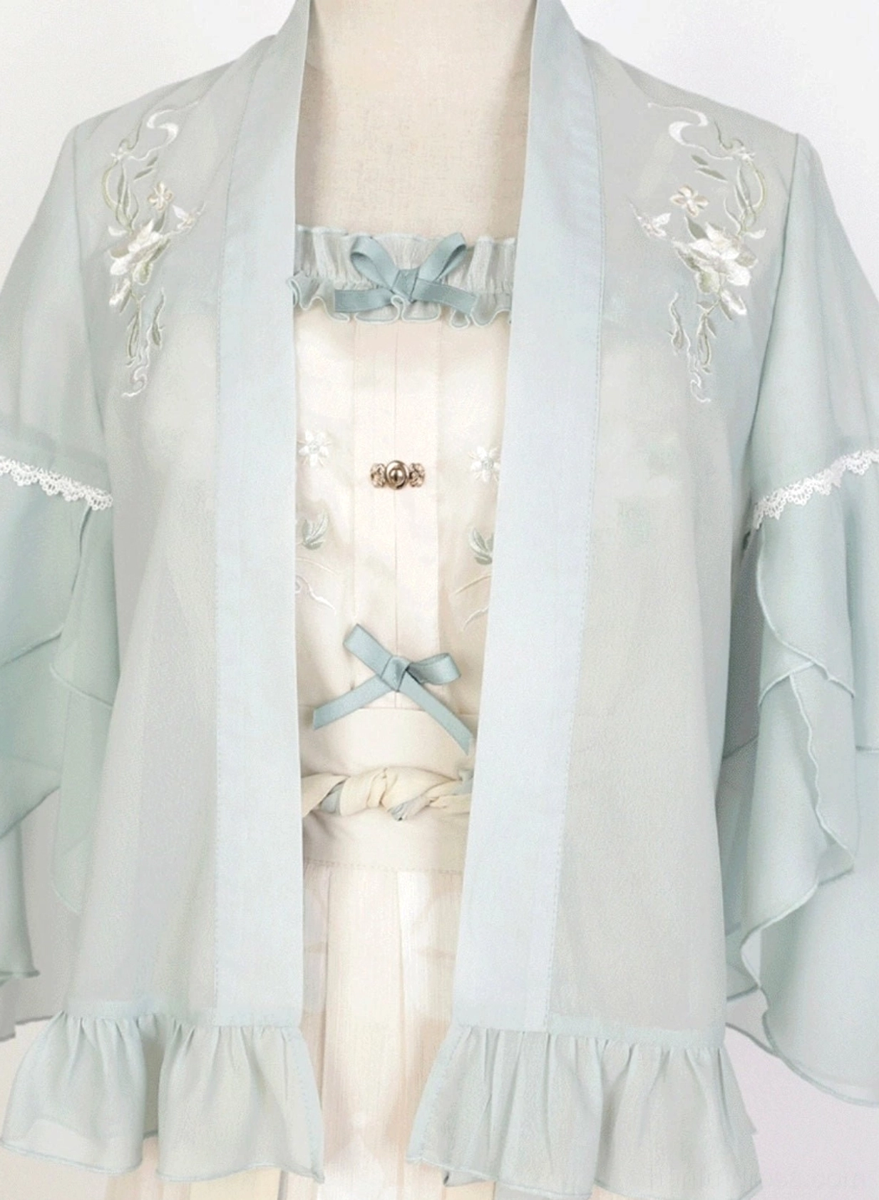 Close-up of mint green chiffon-style Hanfu cardigan with floral shoulder embroidery lace trim ruffled cuffs and off-white camisole bow detail