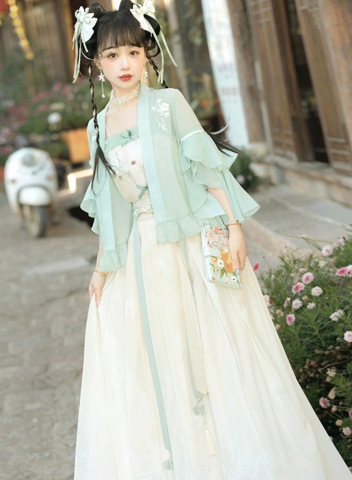Mint green embroidered cardigan and off-white camisole from a modern Song style Hanfu set styled with traditional hair accessories on an ancient town street
