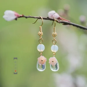 Mint green floral hanfu earrings with pink flower charms milky white beads gold tone spacers and clear teardrop glass pendants displayed on a flowering twig