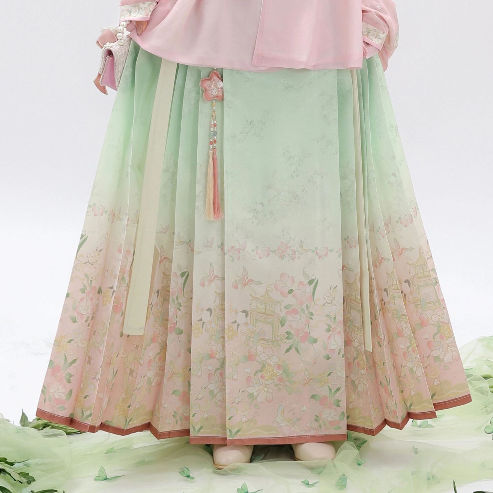 Close-up of mint green to pink floral mamian skirt with pleats tassel waist pendant and embroidered bottom trim