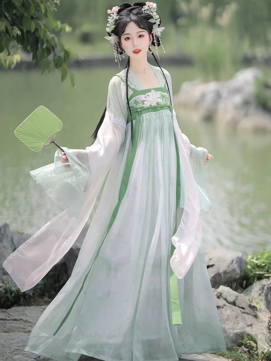 Mint green and blush pink Tang style Qixiong Ruqun Hanfu set in waterside garden, featuring a flowing chiffon skirt, sheer shawl, and green folding fan