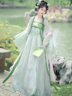Mint green Tang Dynasty Qixiong Ruqun Hanfu dress set front view with pink sheer shawl, floral bust detail, green sashes, folding fan, and traditional Chinese garden background