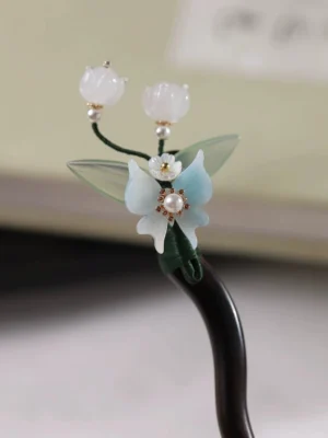 Close-up of handmade Chinese floral hair stick with white bell flowers blue orchid pearl detail and wooden shaft