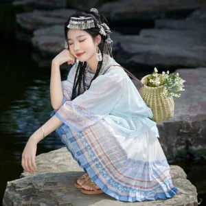 Modern Hanfu outfit with pastel ethnic stripe pleated skirt styled with silver accessories and woven basket beside a Chinese lakeside garden