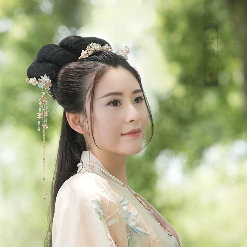 Model wearing colorful spring Chinese hanfu hair accessories with floral crown and matching tassel hairpins in a traditional coiled hairstyle with light yellow hanfu