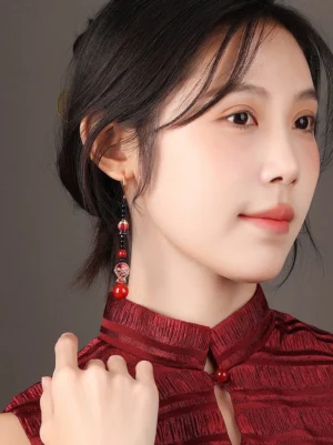 Model wearing scarlet koi fish drop earrings with a dark red textured cheongsam showing the elegant on-ear effect