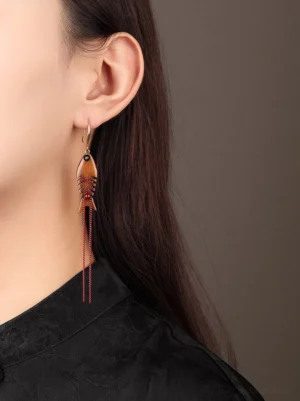 Model wearing dangling wooden fish Chinese earrings with red tassels and a black Chinese stand collar top
