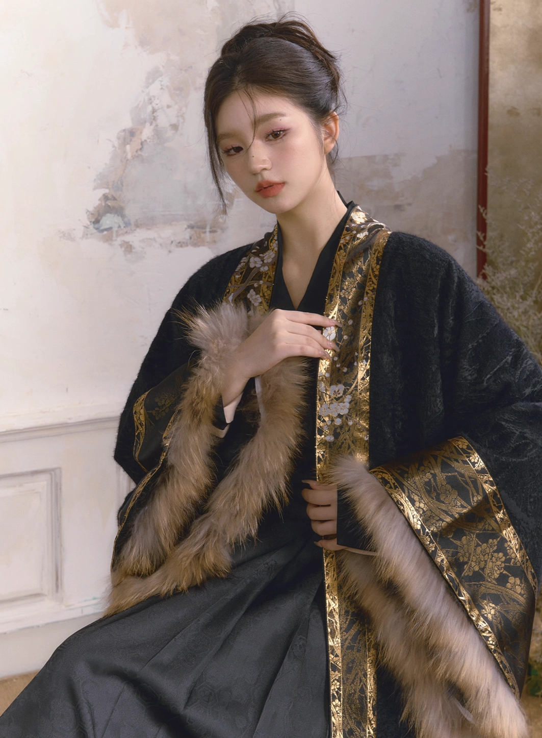 Half body view of a modern Chinese Hanfu coat showing wide sleeves, gold floral front trim, removable fur cuffs, and textured black fabric