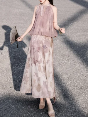 Full front view of a woman wearing a dusty pink modern Chinese Hanfu halter top and flowing ink-print A-line maxi skirt while holding a traditional folding fan outdoors