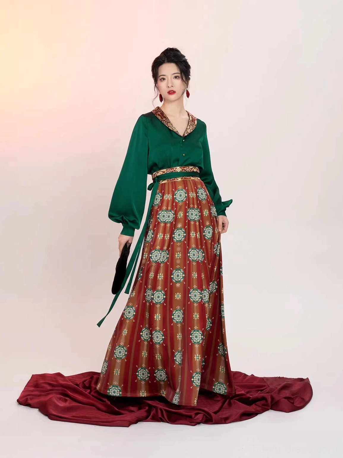 Front three-quarter view of a modern Chinese Hanfu two-piece outfit with embroidered emerald green blouse, matching waist sash, red floral geometric printed wrap skirt, and elegant side silhouette