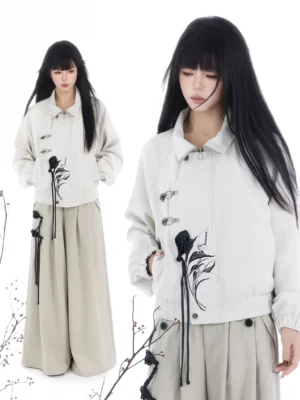 Two models wearing modern Chinese Hanfu cropped jackets with frog closures, black floral embroidery, tassels, and wide-leg pants