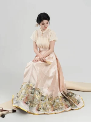 Female model sitting in a modern Chinese hanfu blouse and mamian skirt outfit with apricot pink tones, traditional hair ornament, and landscape printed skirt border