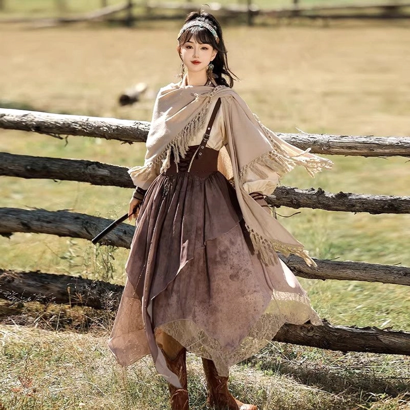 Back half-side view of a modern Chinese Hanfu set showing the flowing irregular lace-trimmed skirt, tasseled shawl, brown layered silhouette, pearl headband, and cowboy boots in a grassy outdoor landscape