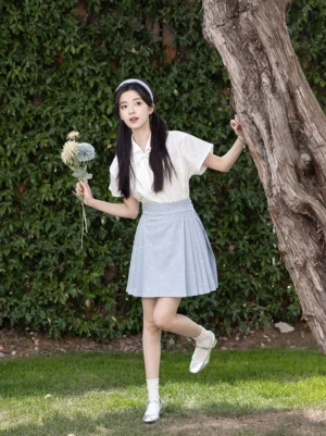Model wearing a modern Chinese hanfu short sleeve top and light blue mini mamianqun horse face skirt set in an outdoor ivy garden