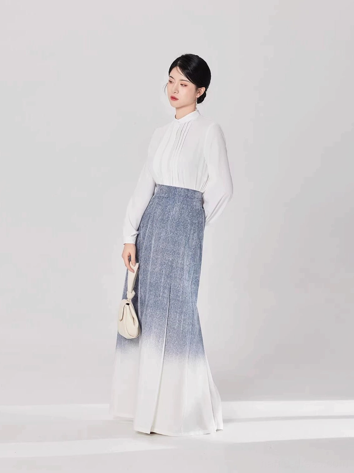 Side view of a modern Chinese style Hanfu outfit with a white blouse, ombre pleated maxi skirt, and beige handbag