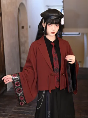 Modern Chinese-style burgundy Hanfu blazer shown from the side with cropped silhouette, notched lapel, wide embroidered cuff, and contemporary layered black skirt styling