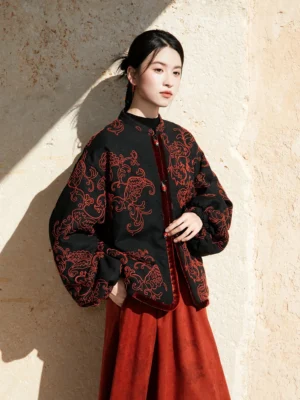 Front three-quarter view of a modern Chinese style Hanfu jacket with red paisley embroidery, velvet placket trim, and beaded buttons
