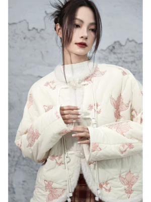 Close three-quarter view of a modern Chinese style cropped jacket showing quilted padded texture, pink koi embroidery, faux fur collar trim, and traditional knot frog buttons