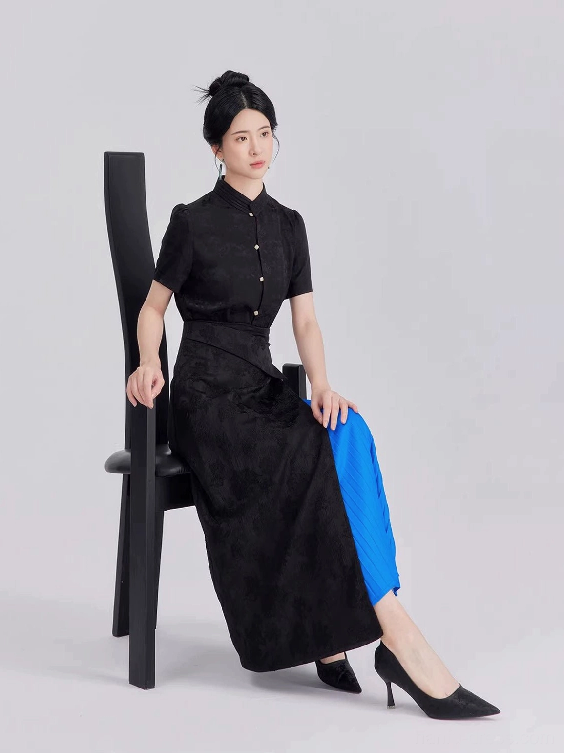 Side seated view of modern Hanfu outfit showing black floral jacquard texture asymmetrical skirt silhouette and contrasting blue pleated detail