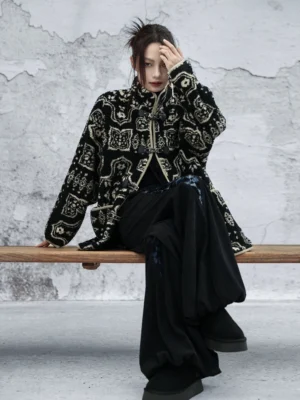 Modern Hanfu black printed coat with beige ancient geometric pattern, stand collar, frog buttons, contrast piping, and relaxed oversized fit shown in a seated three-quarter front view