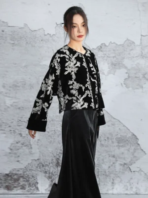 Modern Hanfu black velvet cropped jacket shown from the left three-quarter angle with silver floral embroidery, wide cuffs, and a contemporary Chinese-style silhouette