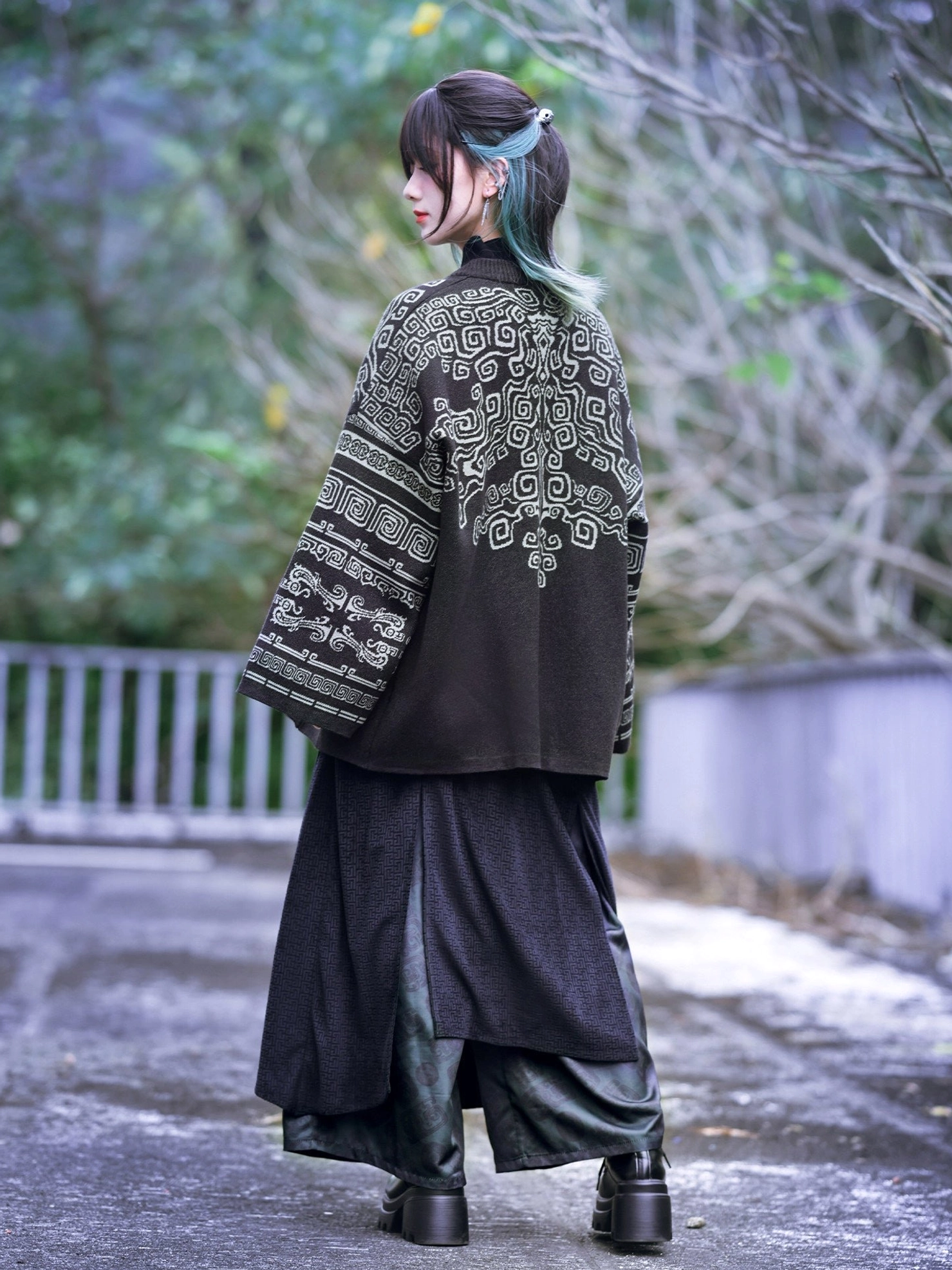 Back three-quarter view showing the complete ancient bronze-inspired texture pattern on a black modern Hanfu cardigan styled with dark wide-leg skirt pants and platform leather shoes