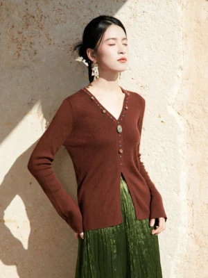Chestnut brown modern Hanfu V-neck knitted sweater cardigan with ribbed texture and decorative gem buttons styled with a green pleated long skirt outdoors