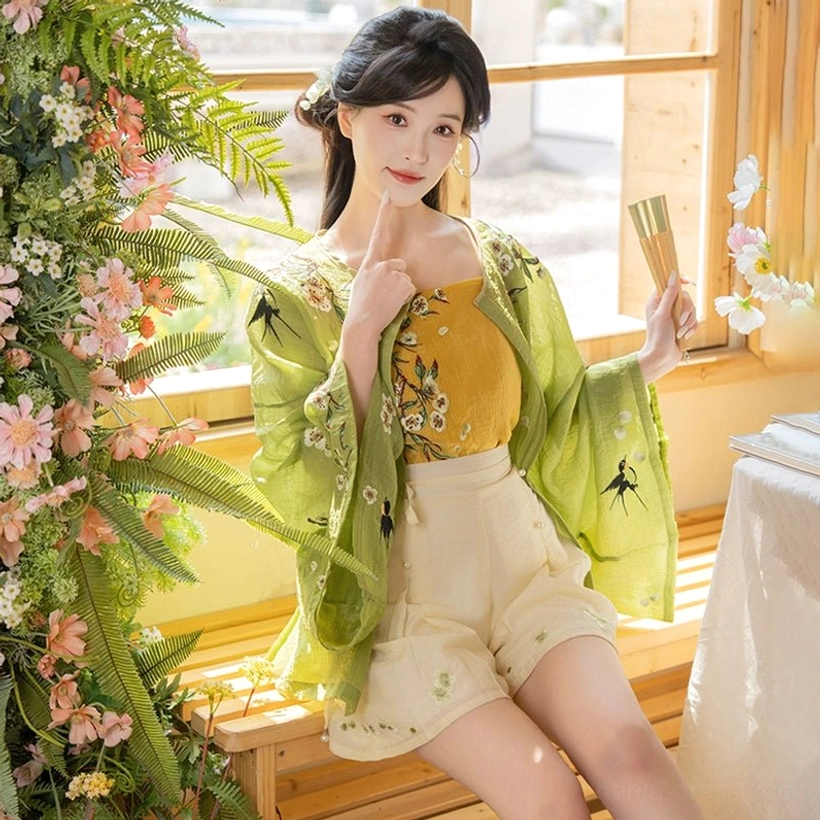 Close up view of delicate bird and floral embroidery on a modern Hanfu cardigan styled with folding fans in warm indoor light