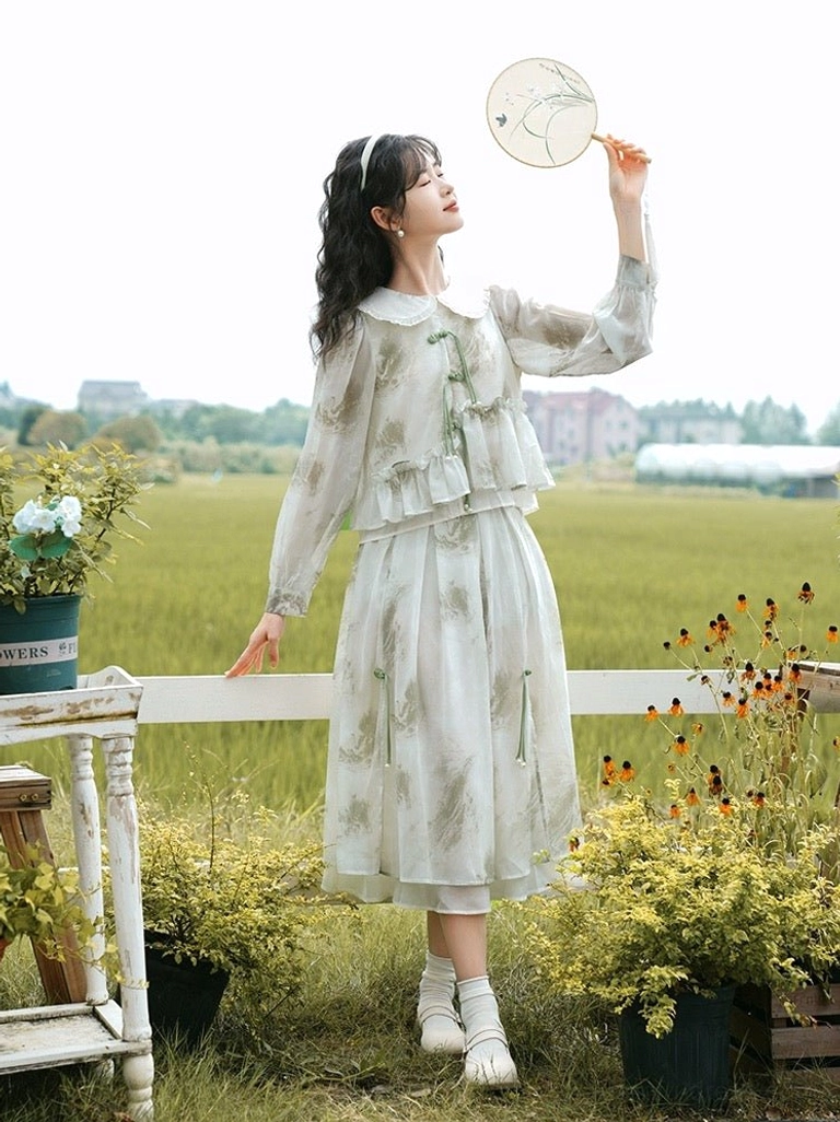 Side view of modern Chinese Hanfu-inspired two-piece dress featuring sheer long sleeves, layered midi skirt, ink-wash plant print, and green tassel decorations