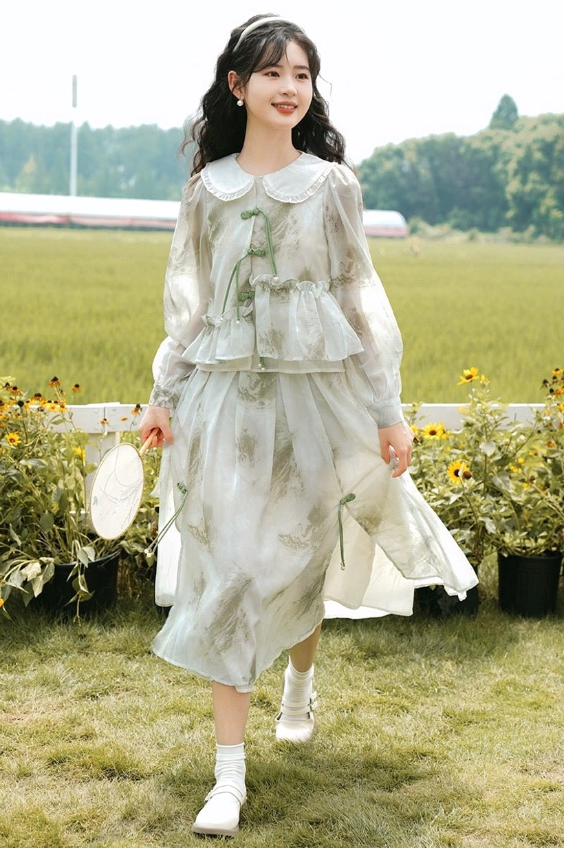 Front full-length view of a modern Hanfu cheongsam two-piece dress with ink botanical print, sheer sleeves, green frog buttons, tassel details, and flowing layered skirt