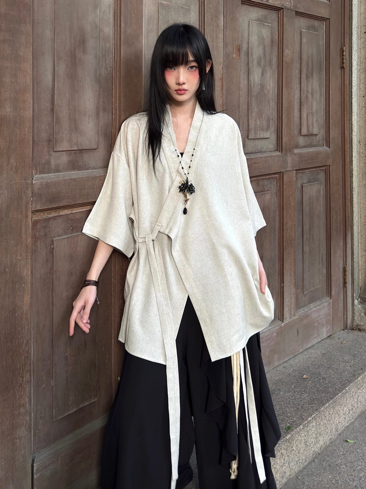Front full-body view of a beige modern Hanfu cross-collar half-sleeve cardigan with textured fabric, oversized fit, and asymmetrical side tie closure