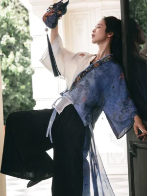 Modern Hanfu cross-collar cardigan and black wide-leg pants outfit shown from a low three-quarter angle with blue and white ink-wash pattern and tied waist sashes