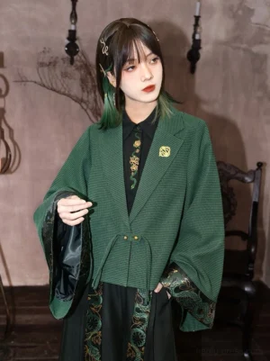 Modern Hanfu dark green cropped wide sleeve jacket worn by model in a vintage interior, featuring textured check fabric, front tie closure, embroidered cuffs and metallic brooch detail
