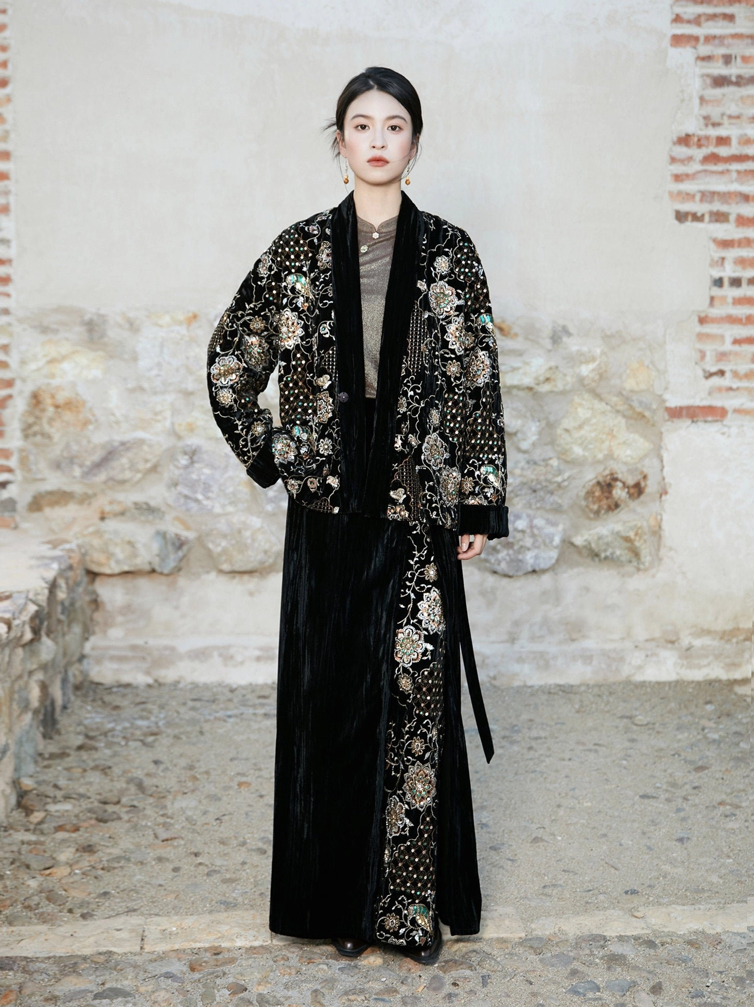 Full front view of coordinated modern Hanfu embroidered jacket and black velvet wrap skirt with side tie waist in a stone courtyard