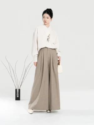 Full-body front view of a woman wearing a modern Hanfu embroidered off-white cross-collar shirt with khaki high-waisted wide-leg pants in a minimalist studio