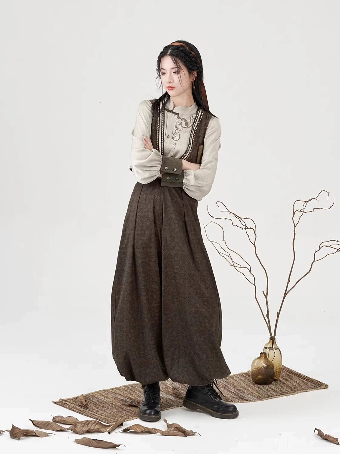 Three-quarter view of a woman wearing a brown embroidered vest, cream long-sleeve Hanfu blouse, and modern lantern pants